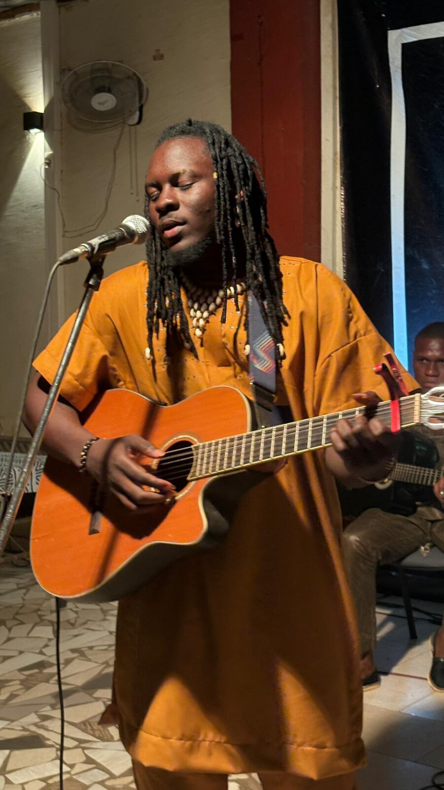 Kalifa Sanou, alias Kalidjo Guitare
Né le 7 octobre 1999 à Dialakorodji Kognoumani/Bamako, Kalifa Sanou, mieux connu sous le nom de scène Kalidjo Guitare, incarne l’essence même de la richesse musicale malienne. Issu d’une famille où la musique est un véritable art de vivre, Kalidjo a été façonné dès son plus jeune âge par des rythmes et des sons ancestraux. Balafon, Kamalé Goni, Djembé, Tamani et, bien entendu, guitare : il maîtrise avec une aisance déconcertante des instruments aussi divers que puissants, hérités d’une tradition musicale qui s’étend bien au-delà des frontières du Mali.
Cependant, ce jeune prodige n’est pas seulement un musicien de génie, mais aussi un chanteur, auteur et compositeur dont la vision artistique dépasse les frontières du traditionnel. En 2015, mû par un désir inébranlable de faire entendre sa voix, il choisit de consacrer sa vie à la musique, s’engageant pleinement sur la scène musicale malienne. Sa passion pour les sonorités authentiques et son approc
